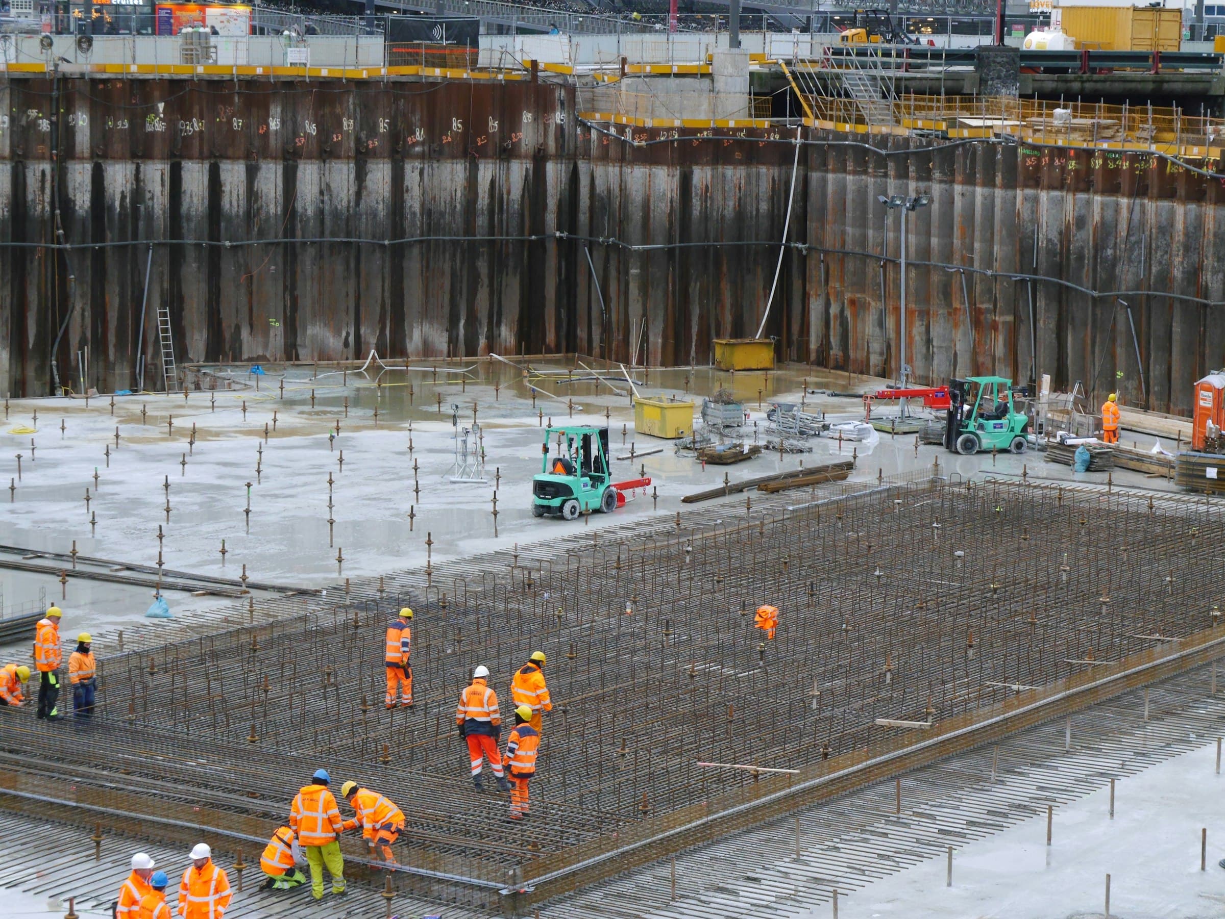 Crew fixing reinforcement across a foundation raft inside a shored excavation