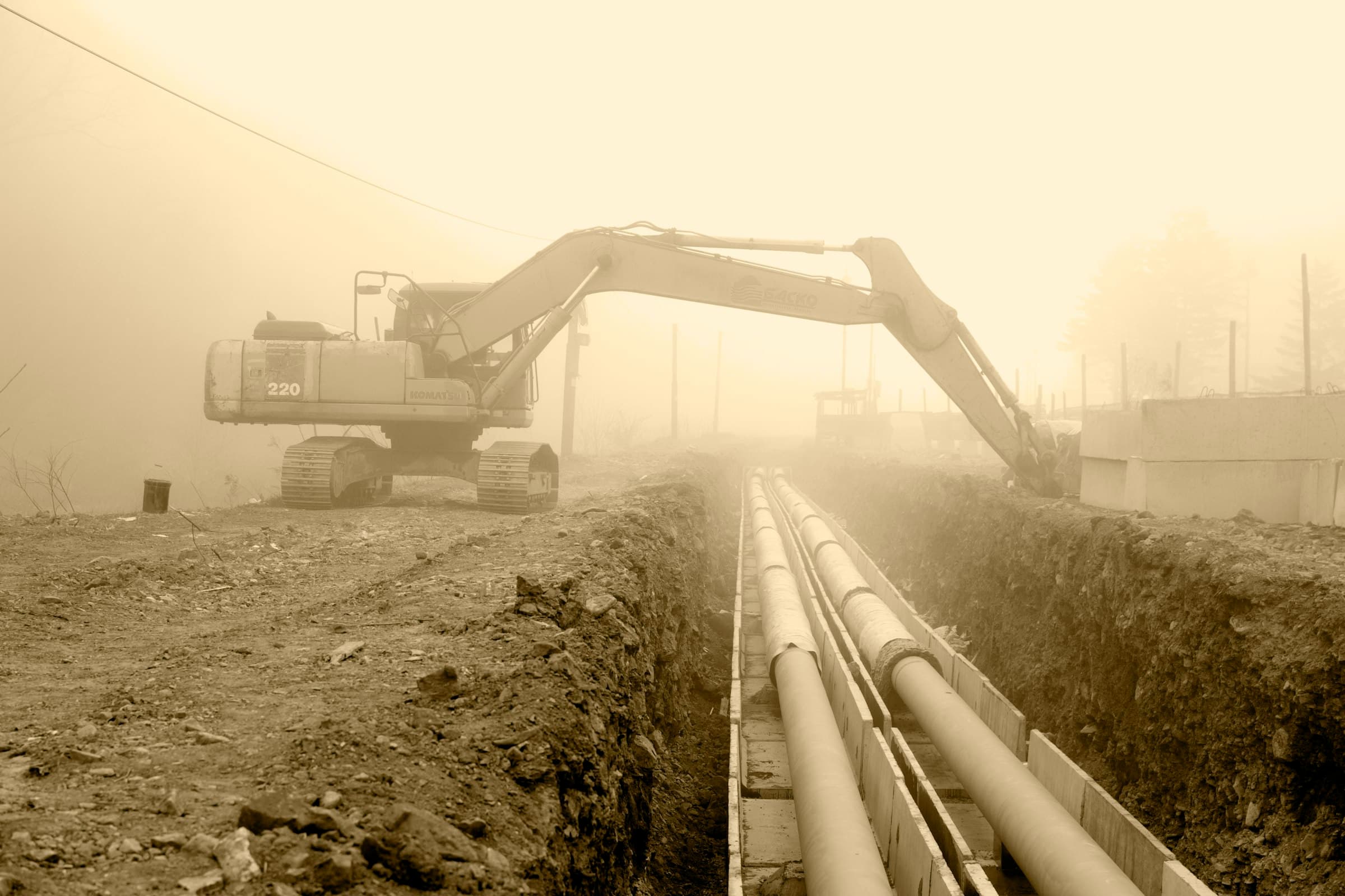 Excavator laying large pipes along an open trench