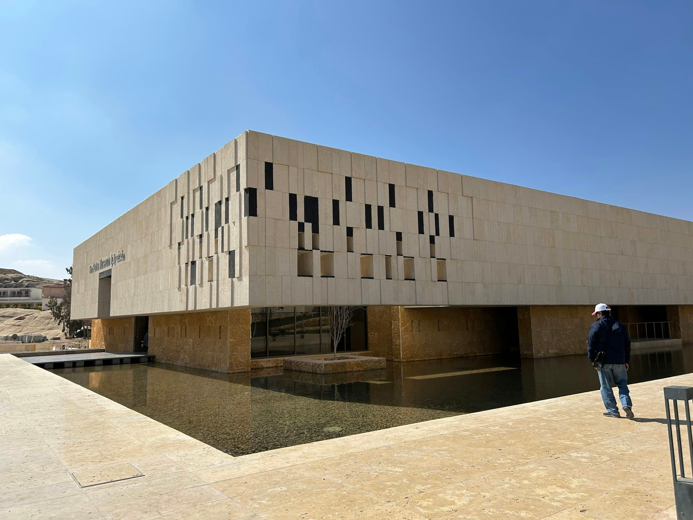 Stone-clad building with a reflecting pool under a clear desert sky