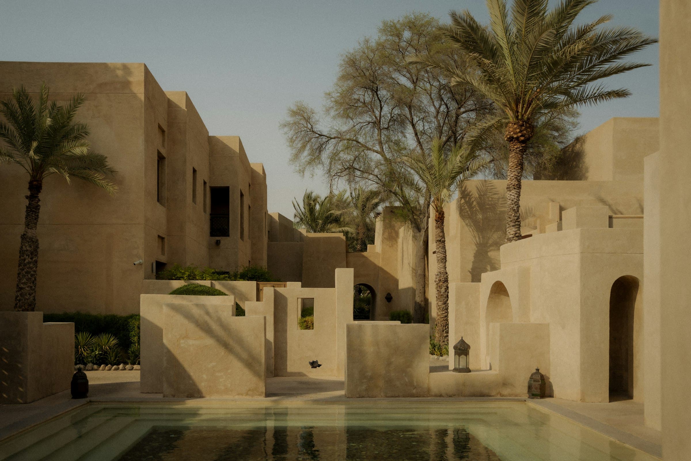 Stone resort buildings among palms around a courtyard pool